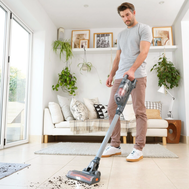 Man using BLACK+DECKER cordless stick vacuum on tile floor